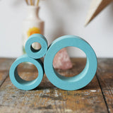 Papoose Toys nesting tubes in earth blue stacked on a wooden desk. 