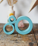 Papoose Toys nesting tubes in earth blue stacked on a wooden desk. 