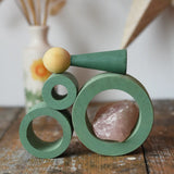Papoose Toys nesting tubes in earth green stacked on a wooden desk with peg doll and a crystal placed on them.