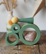 Papoose Toys nesting tubes in earth green stacked on a wooden desk with peg doll and a crystal placed on them.