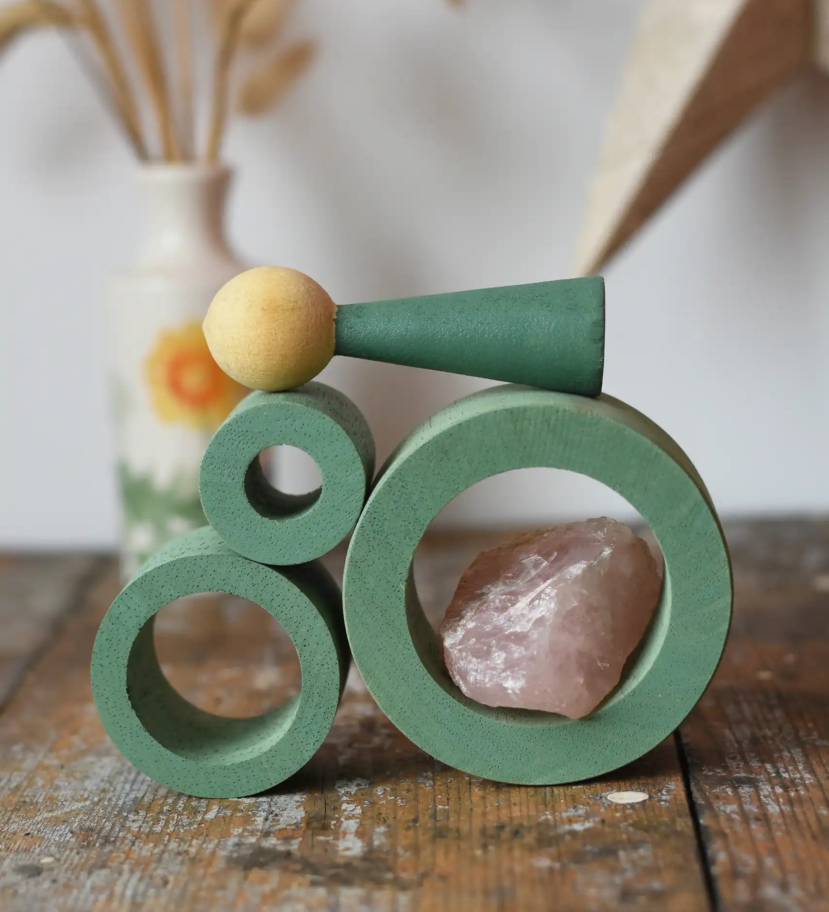 Papoose Toys nesting tubes in earth green stacked on a wooden desk with peg doll and a crystal placed on them.