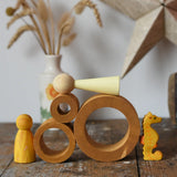 Papoose Toys nesting tubes in earth yellow on a wooden desk with toys placed on and around them. 