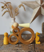 Papoose Toys nesting tubes in earth yellow on a wooden desk with toys placed on and around them. 