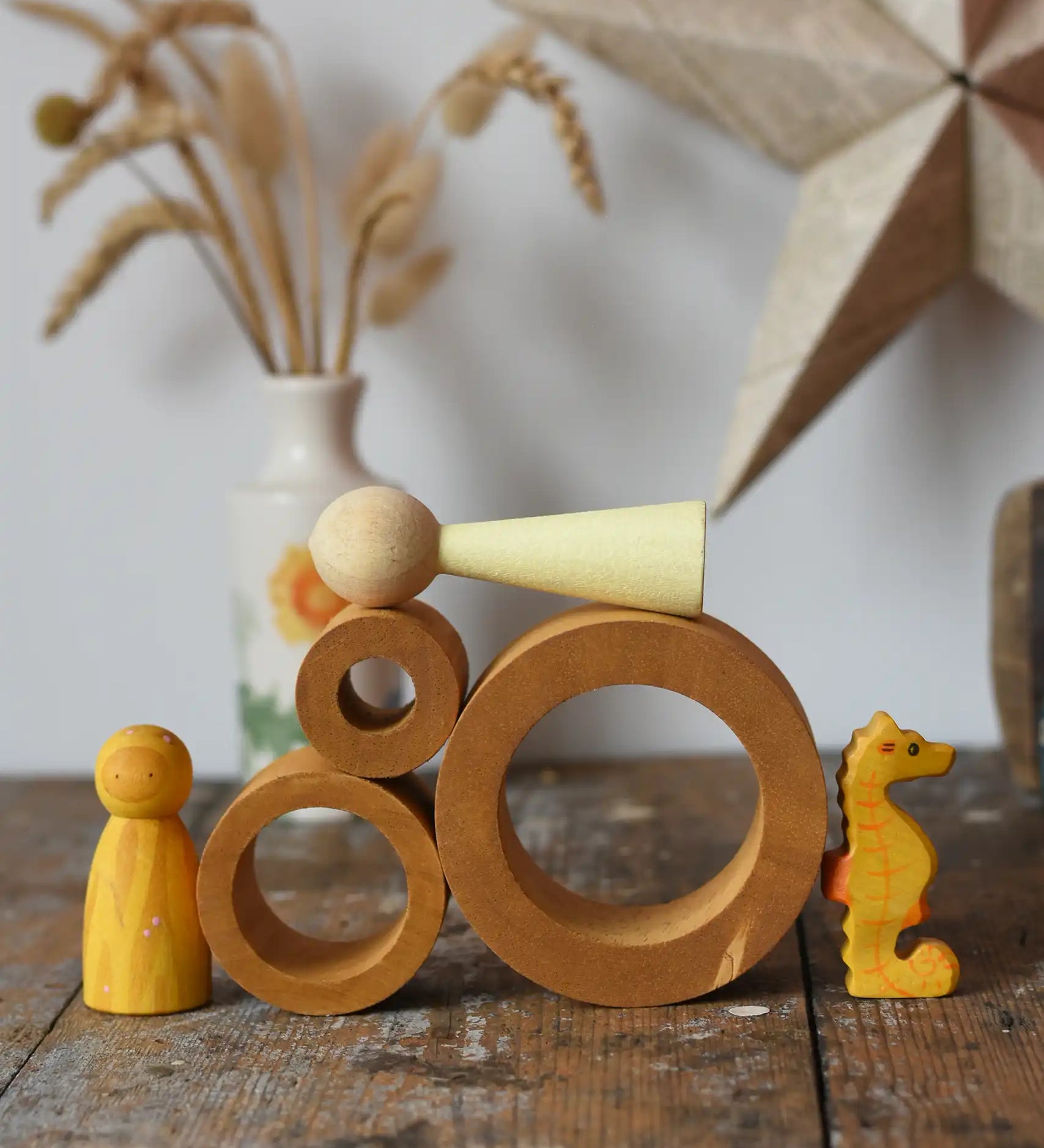 Papoose Toys nesting tubes in earth yellow on a wooden desk with toys placed on and around them. 
