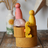 Papoose Toys nesting tubes in earth yellow stacked up on a wooden desk with toys on them. 