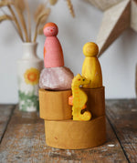 Papoose Toys nesting tubes in earth yellow stacked up on a wooden desk with toys on them. 
