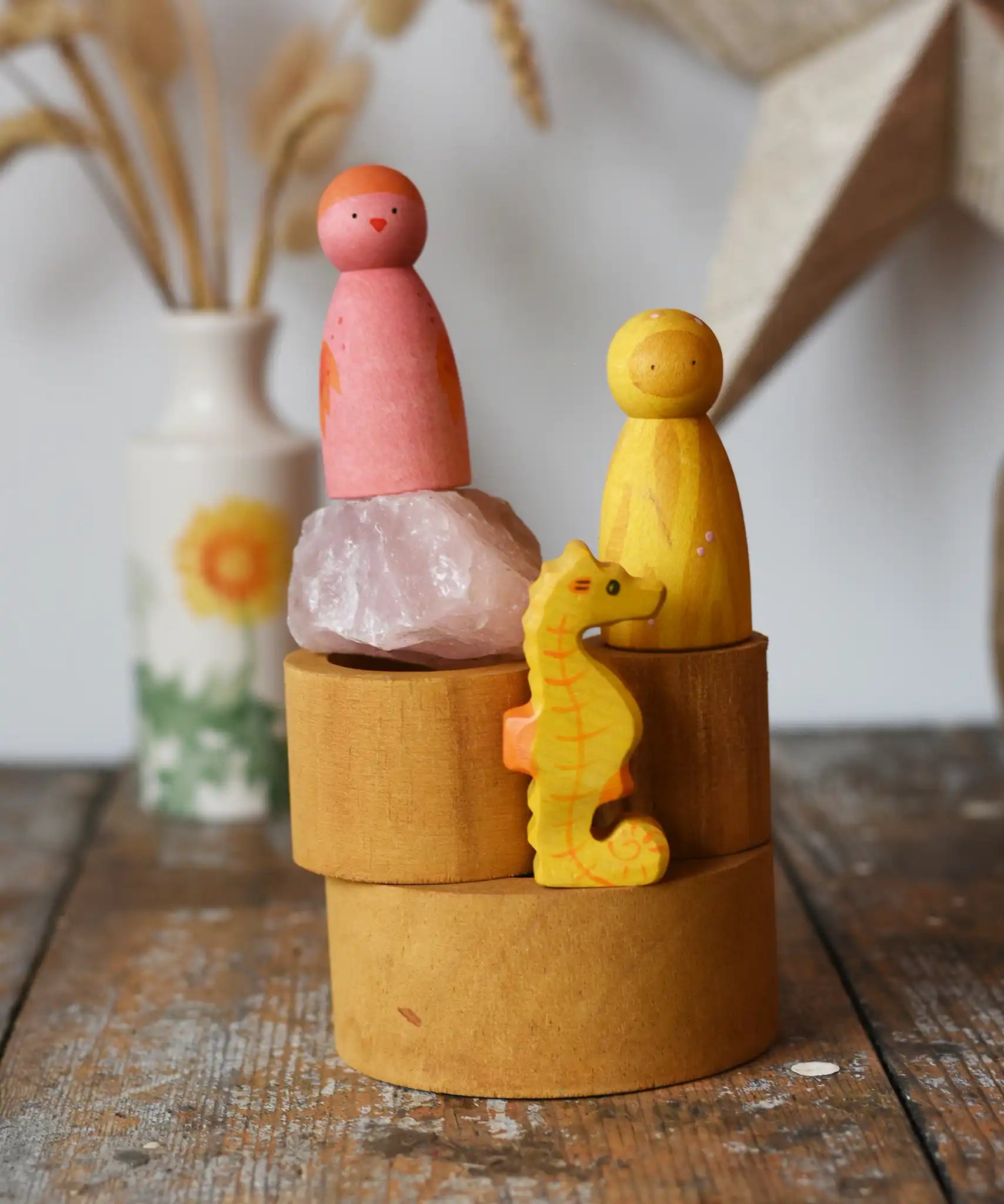 Papoose Toys nesting tubes in earth yellow stacked up on a wooden desk with toys on them. 