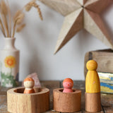Papoose Toys nesting tubes natural wooden rings placed on a wooden desk with wild crew peg dolls placed on and in them. 