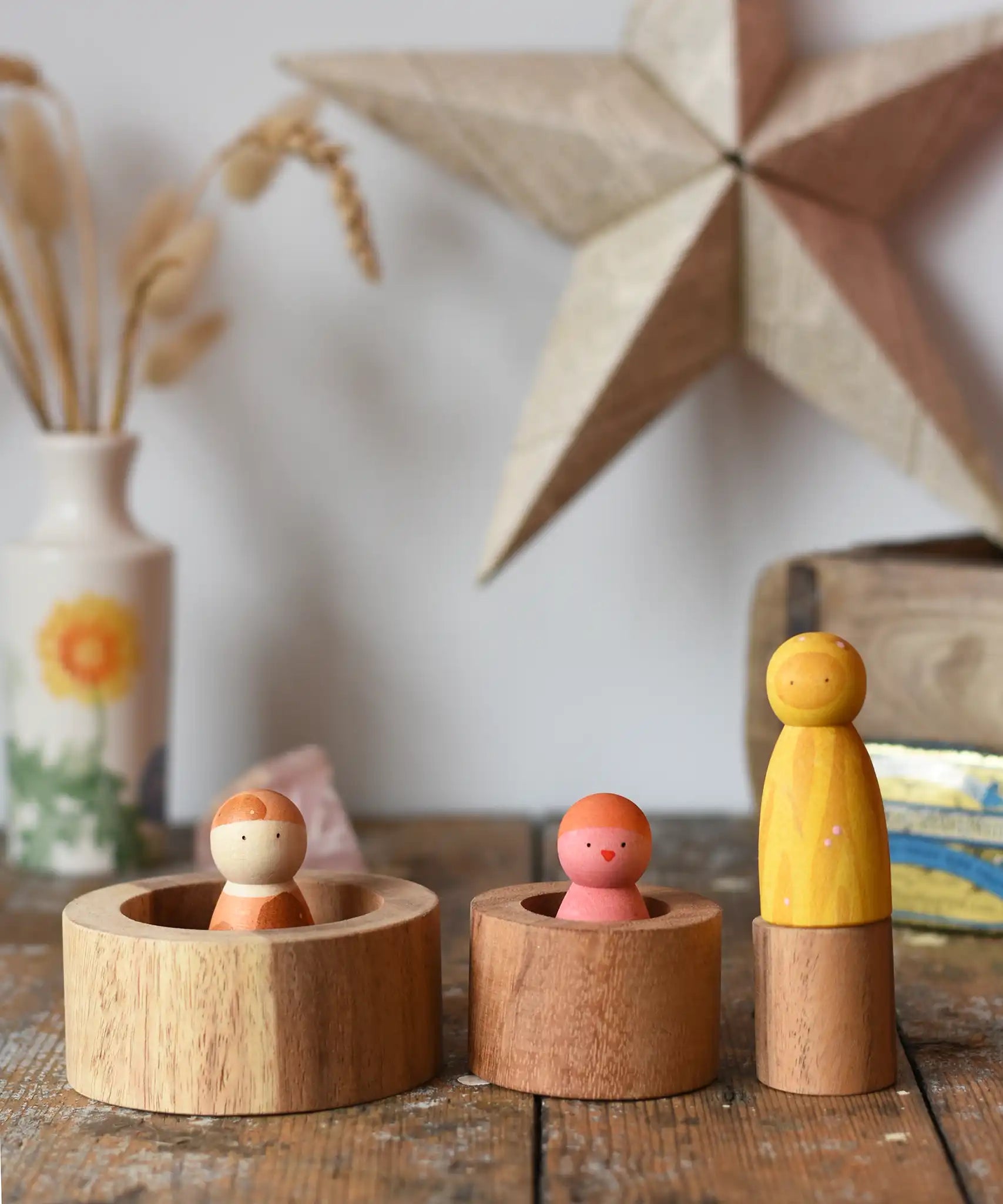Papoose Toys nesting tubes natural wooden rings placed on a wooden desk with wild crew peg dolls placed on and in them. 