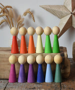 Papoose Toys 12 wooden Goethe rainbow people peg dolls placed on a wooden desk.