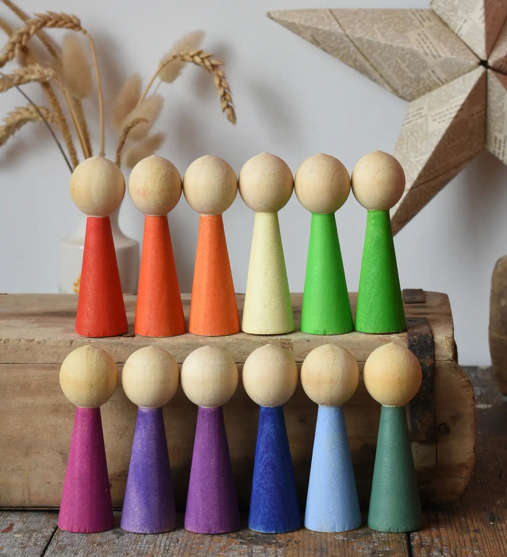 Papoose Toys 12 wooden Goethe rainbow people peg dolls placed on a wooden desk.