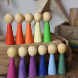 Papoose Toys 12 wooden Goethe rainbow people peg dolls placed on a wooden desk.