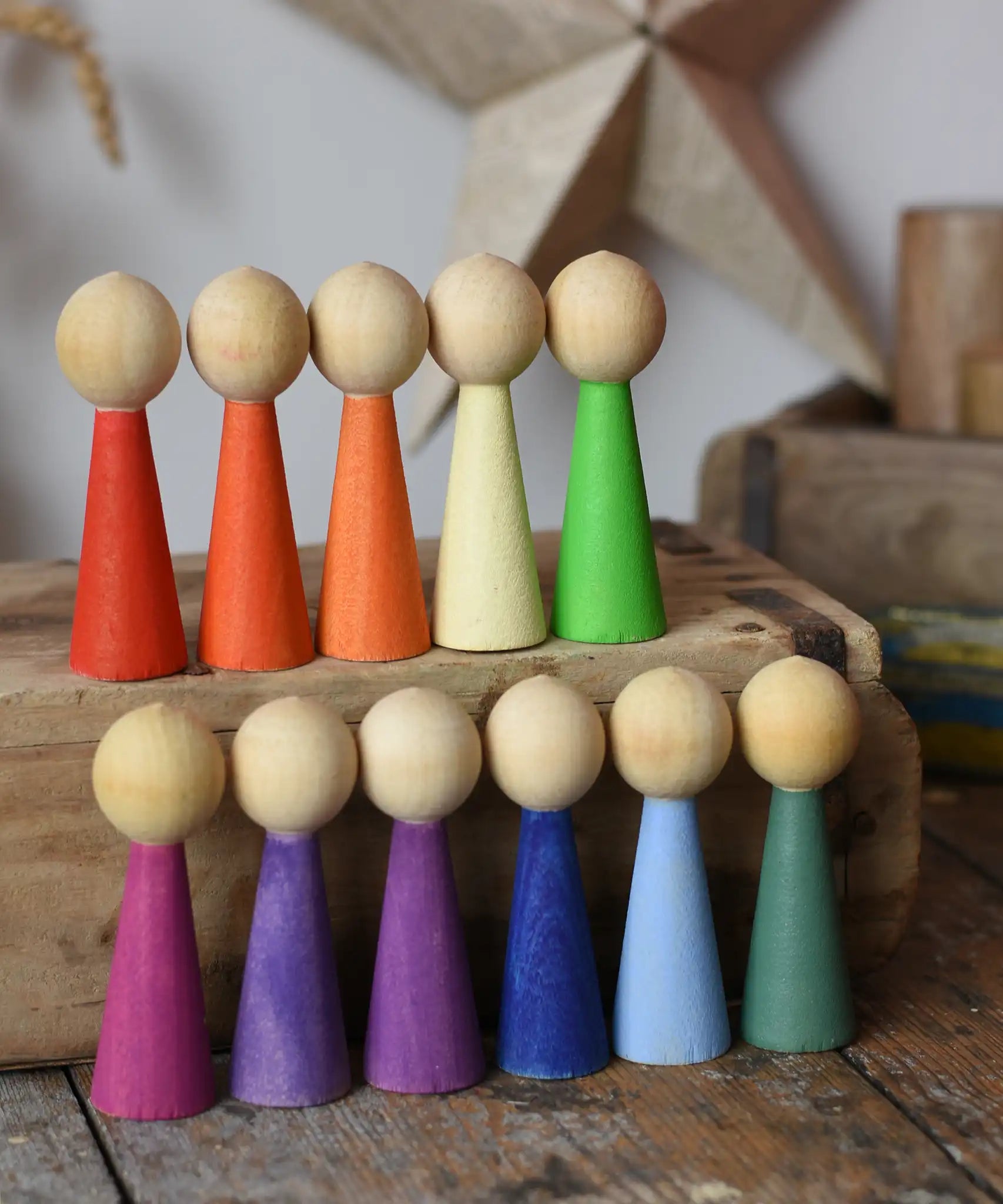 Papoose Toys 12 wooden Goethe rainbow people peg dolls placed on a wooden desk.