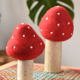 Papoose Toys felt toadstool wooden toy set placed on a rattan top stool. 