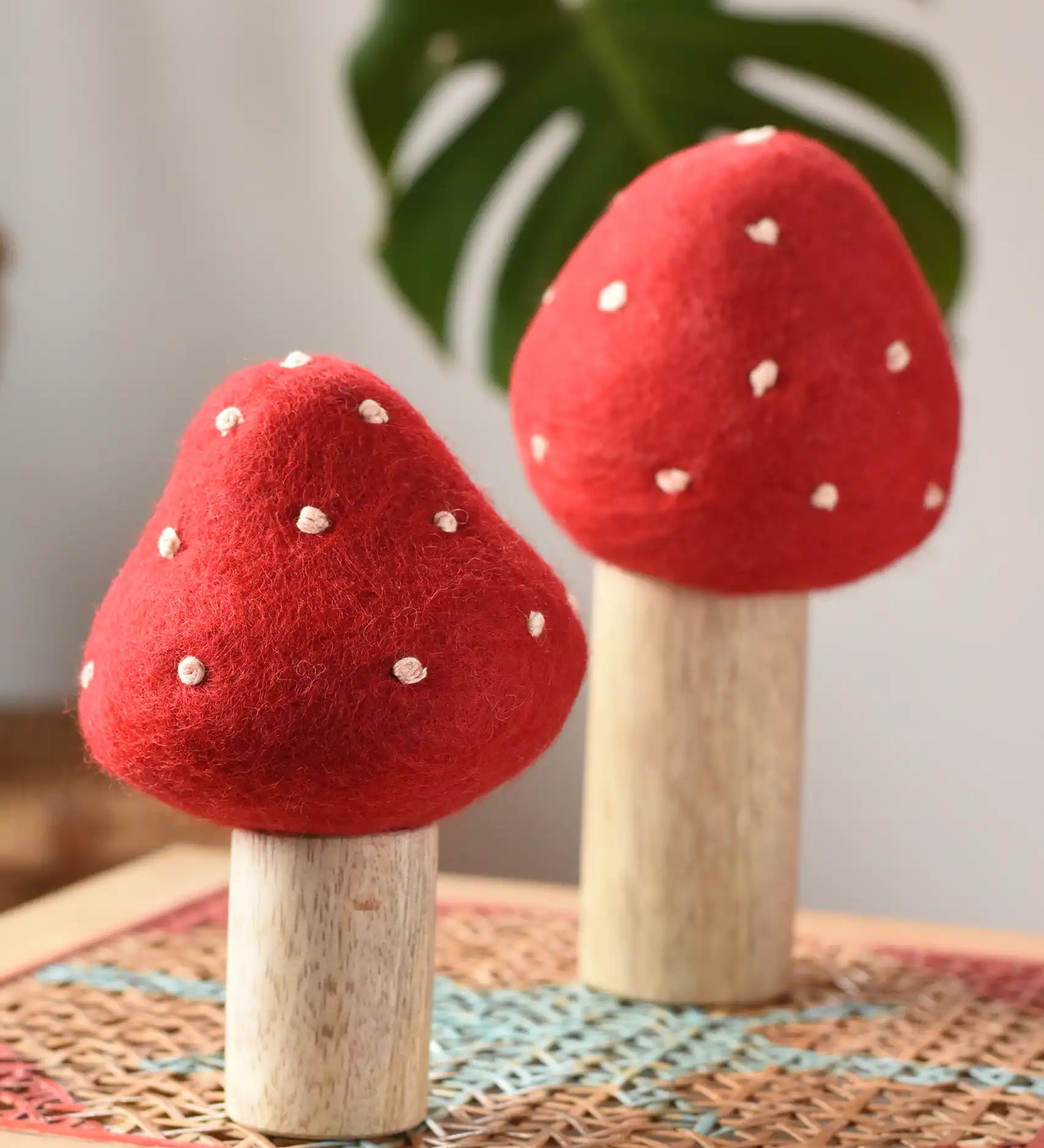 Papoose Toys felt toadstool wooden toy set placed on a rattan top stool. 