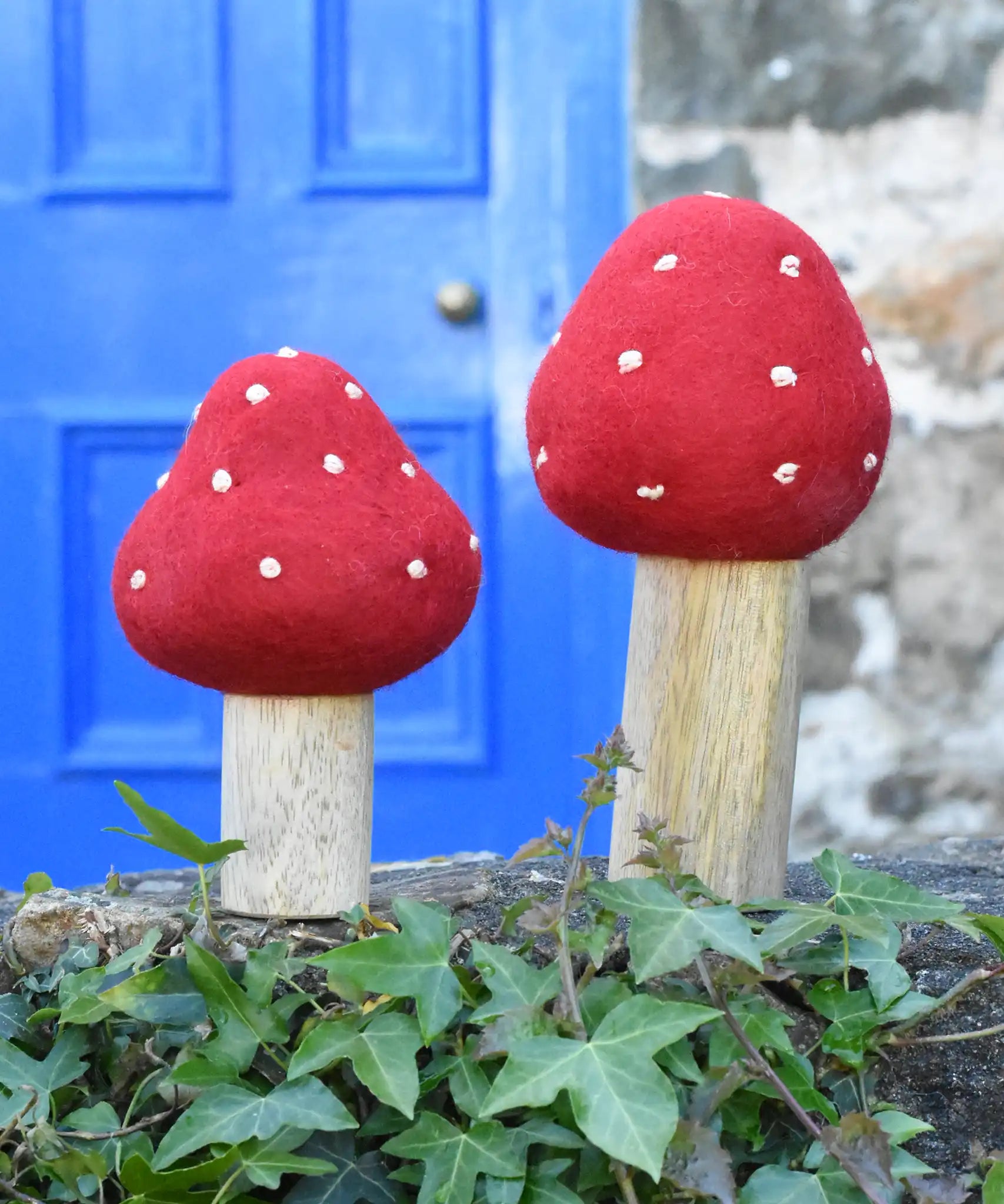 Papoose Toys felt toadstool wooden toy set placed on stone wall outdoors.