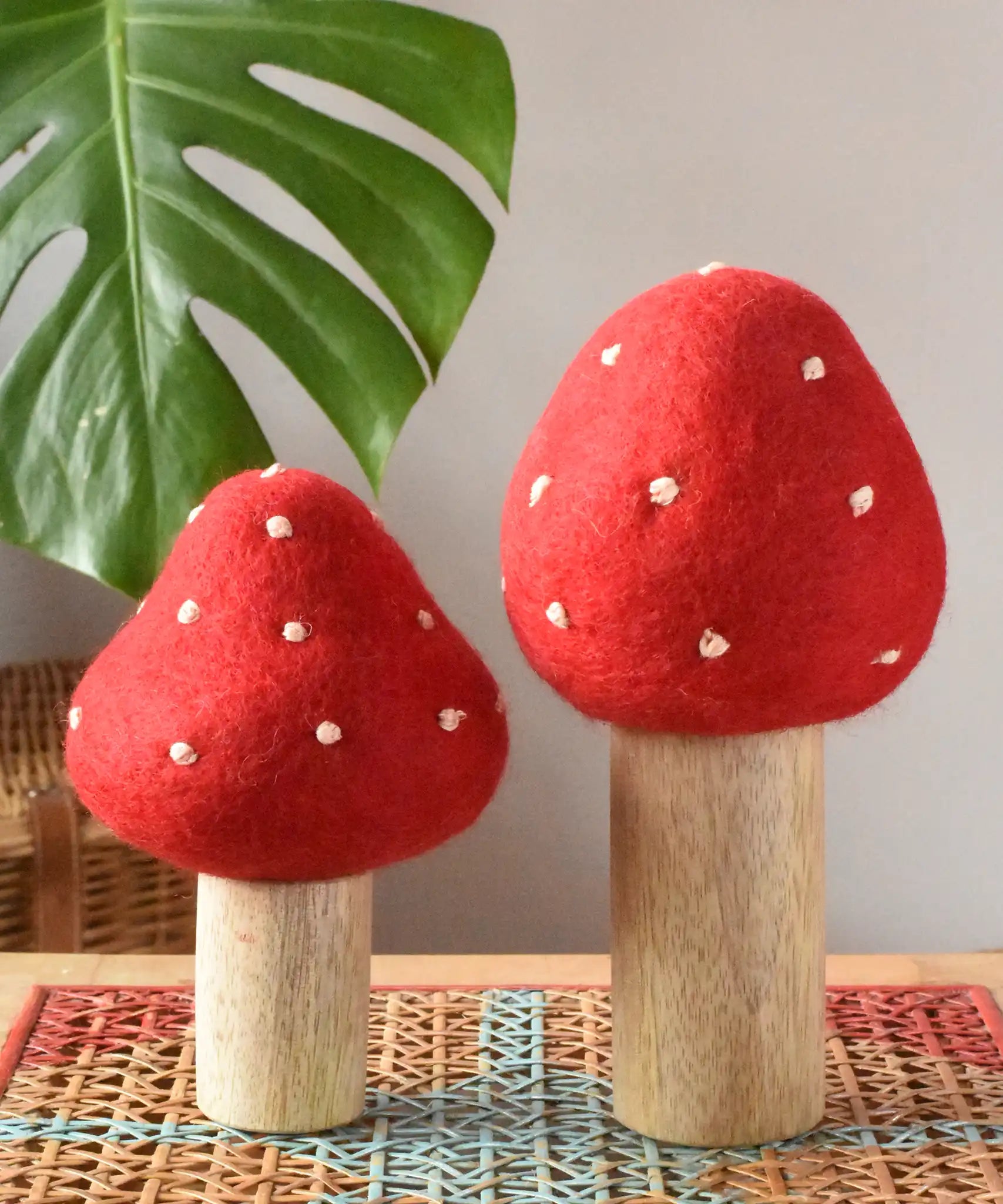 Papoose Toys felt toadstool wooden toy set placed on a rattan top stool. 