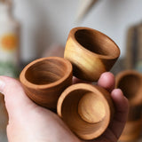 Three bowls from the Papoose Toys 12 small natural wooden bowls set in an adult's hand.
