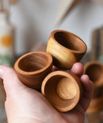 Three bowls from the Papoose Toys 12 small natural wooden bowls set in an adult's hand.