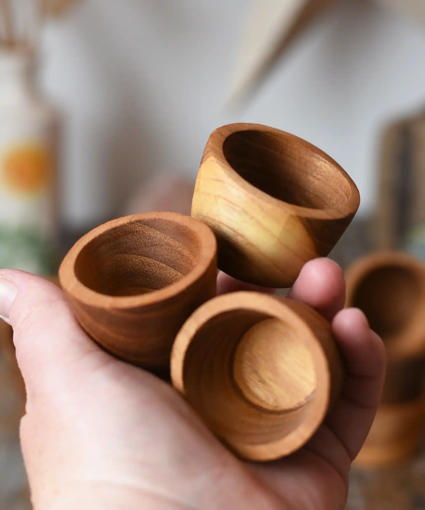 Three bowls from the Papoose Toys 12 small natural wooden bowls set in an adult's hand.
