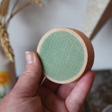 Green Papoose Toys wooden earth coin in an adult's hand.