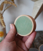 Green Papoose Toys wooden earth coin in an adult's hand.
