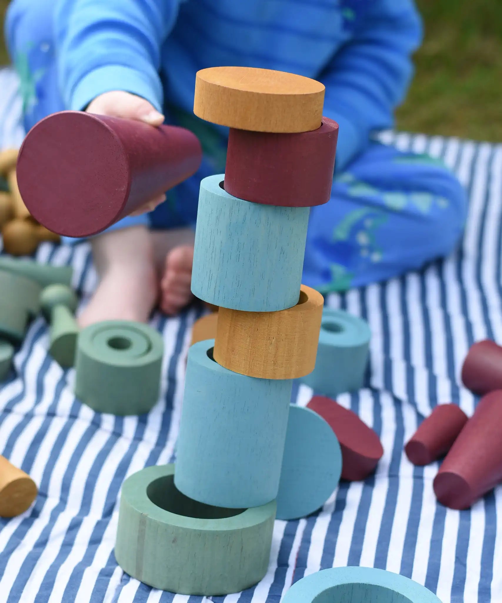 Rubes and discs from the Papoose Toys wooden earth tinker tray school set stacked up. Child knocking them down using the large red cone.