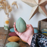 Green pebble from the Papoose Toys earth wooden pebbles set in an adult's hand.