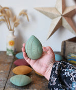 Green pebble from the Papoose Toys earth wooden pebbles set in an adult's hand.