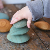 Three green pebbles from the Papoose Toys earth wooden pebbles  stacked on top of each other.