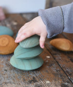 Three green pebbles from the Papoose Toys earth wooden pebbles  stacked on top of each other.