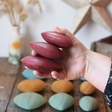 Three red pebbles from the Papoose Toys earth wooden pebbles set in an adult's hand.