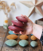 Three red pebbles from the Papoose Toys earth wooden pebbles set in an adult's hand.