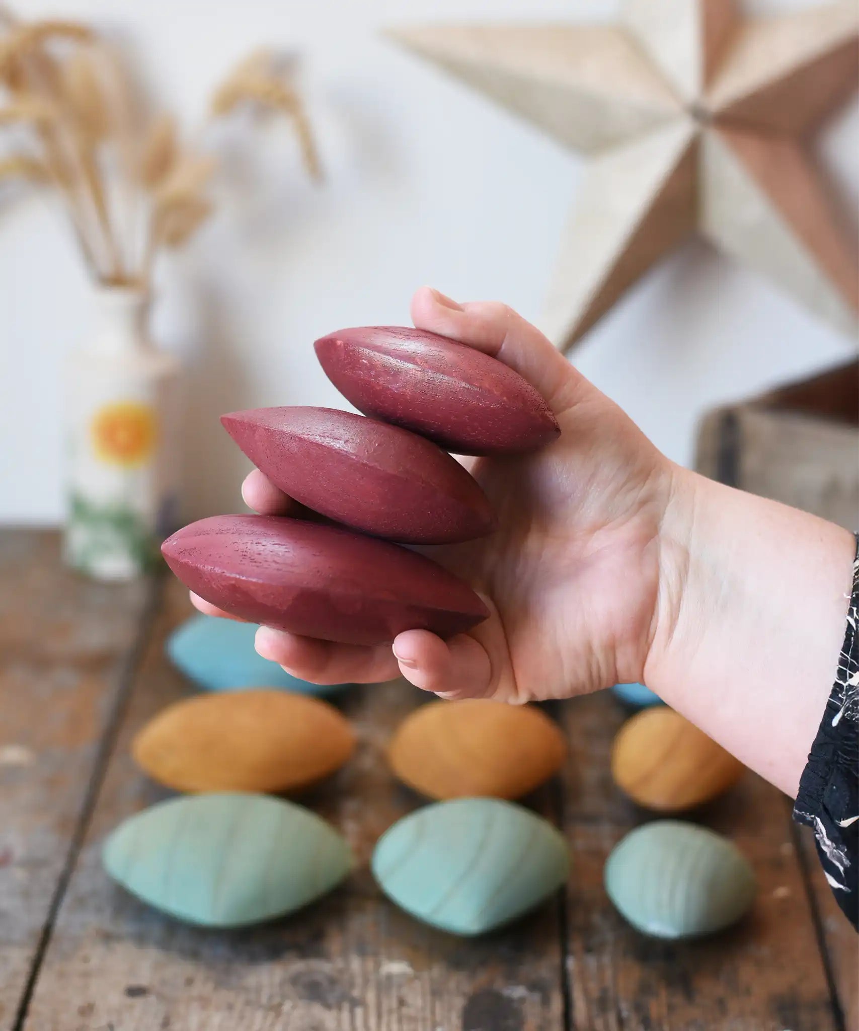 Three red pebbles from the Papoose Toys earth wooden pebbles set in an adult's hand.