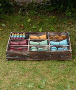 Papoose Toys wooden earth tinker tray school set placed on grass outdoors. The rustic look tray is filled with yellow, red, green and blue earth toned wooden toys and loose parts. 