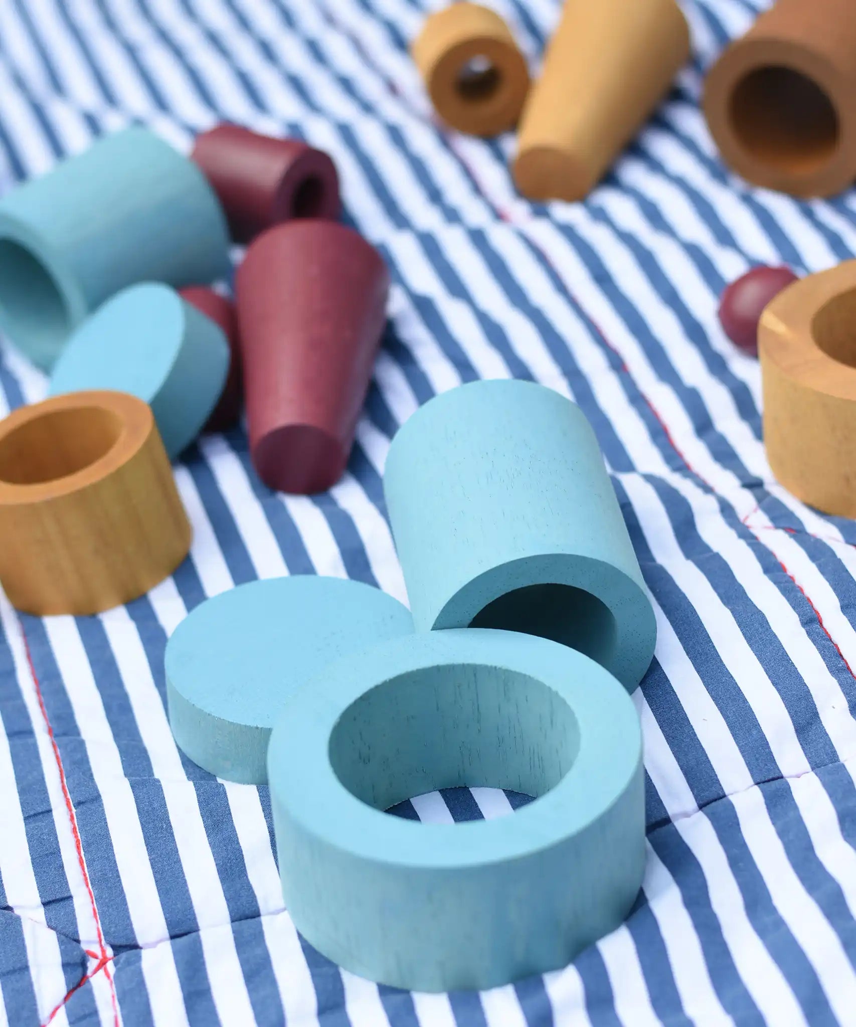 Blue peces from the Papoose Toys wooden earth tinker tray school set placed on a striped blanket.