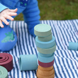 Stacking discs from the Papoose Toys wooden earth tinker tray school set stacked up on a striped blanket. 
