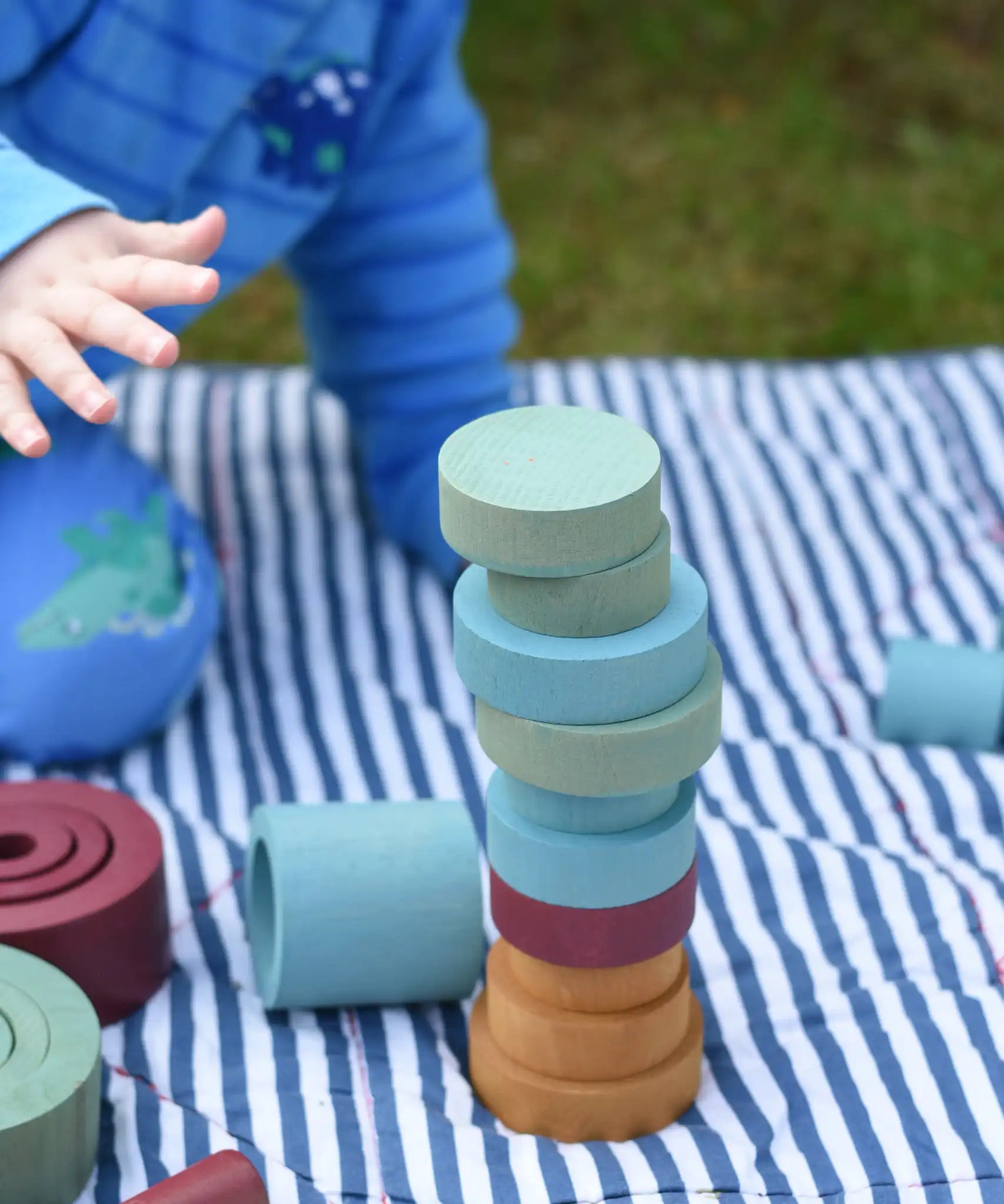 Stacking discs from the Papoose Toys wooden earth tinker tray school set stacked up on a striped blanket. 