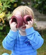 Child holding two pieces from the red earth Papoose Nesting tubes up to his eyes.