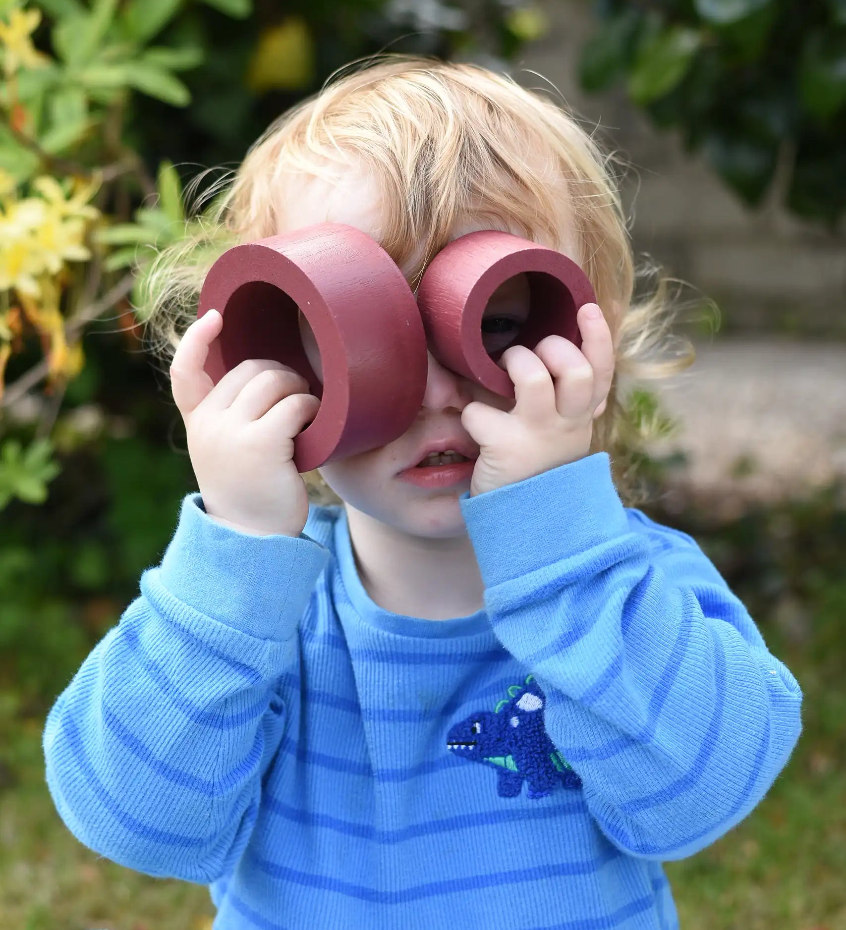 Child holding two pieces from the red earth Papoose Nesting tubes up to his eyes.