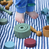 Papoose Toys wooden earth tinker tray school set pieces placed on a striped blanket, a child is standing on the blanket.