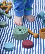 Papoose Toys wooden earth tinker tray school set pieces placed on a striped blanket, a child is standing on the blanket.