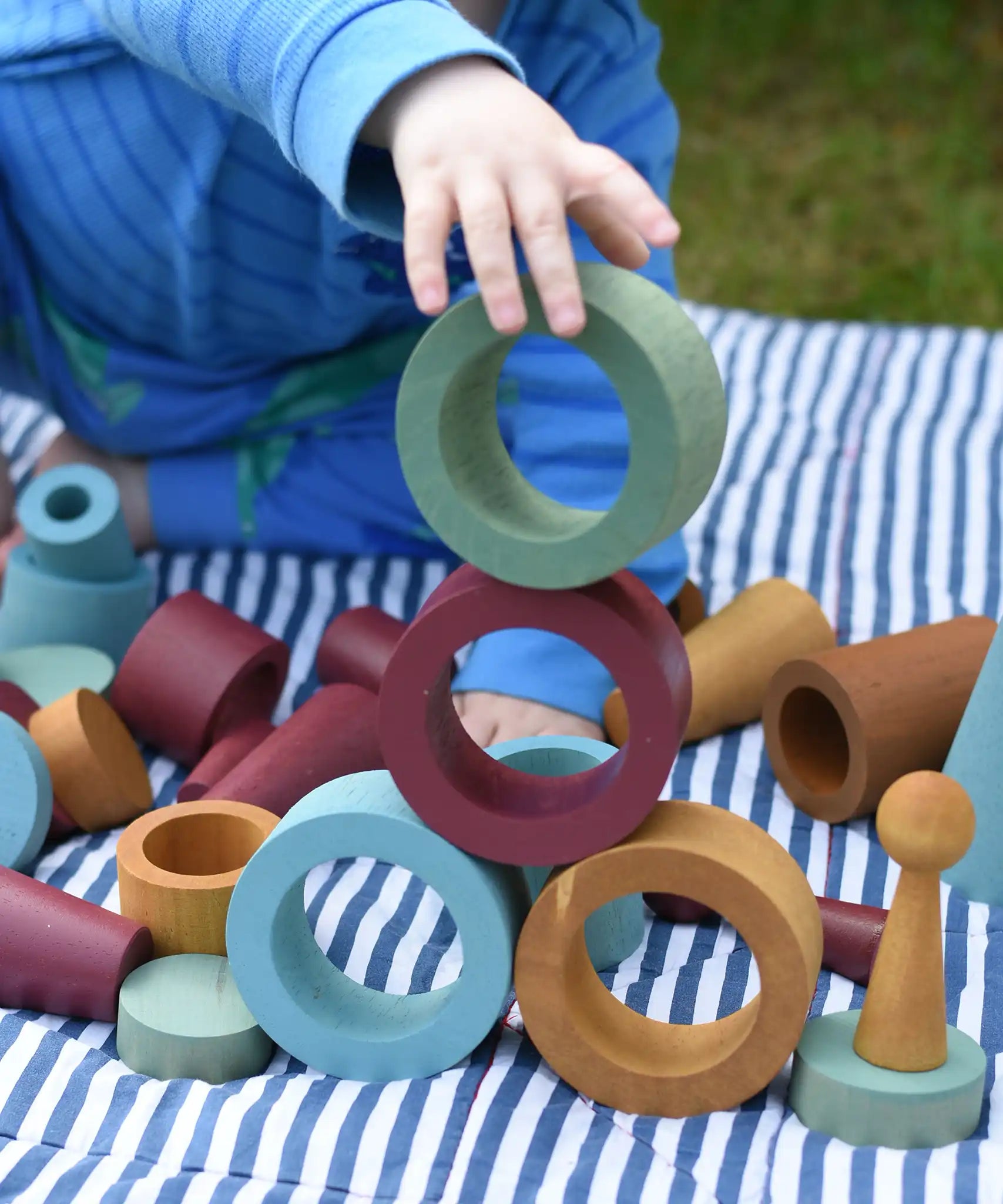 Child stacking and balancing earth coloured wooden tubes on top of each other.