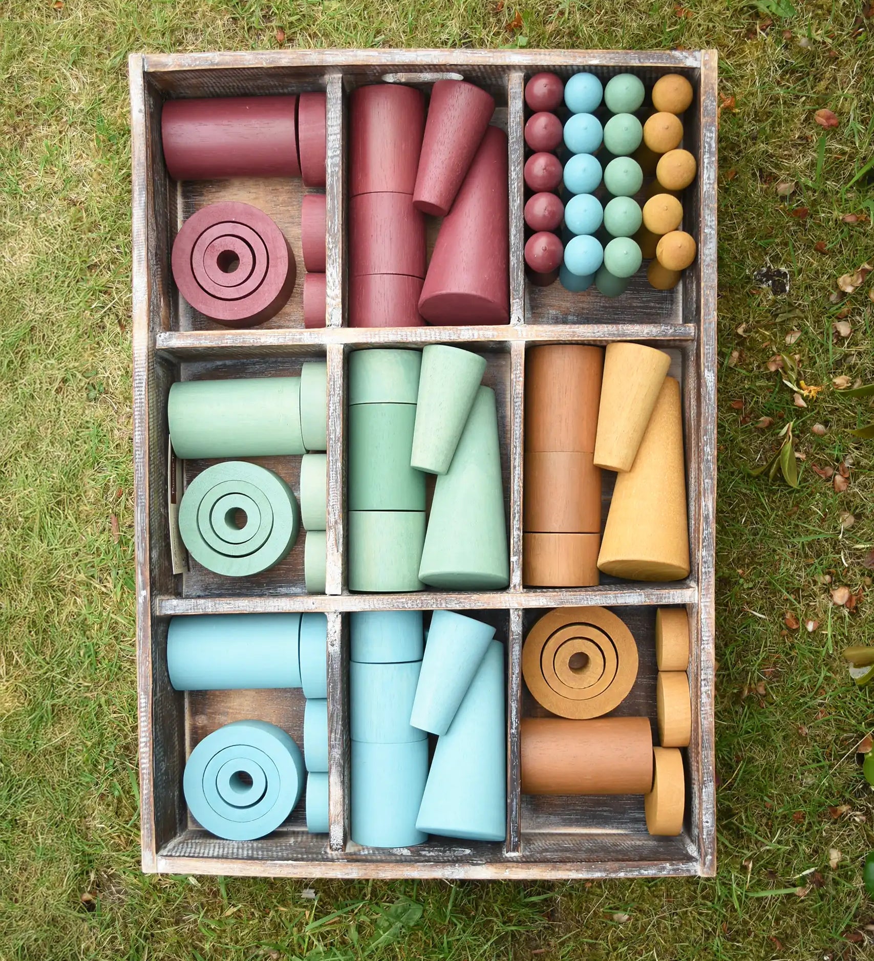 Papoose Toys wooden earth tinker tray school set placed on grass.