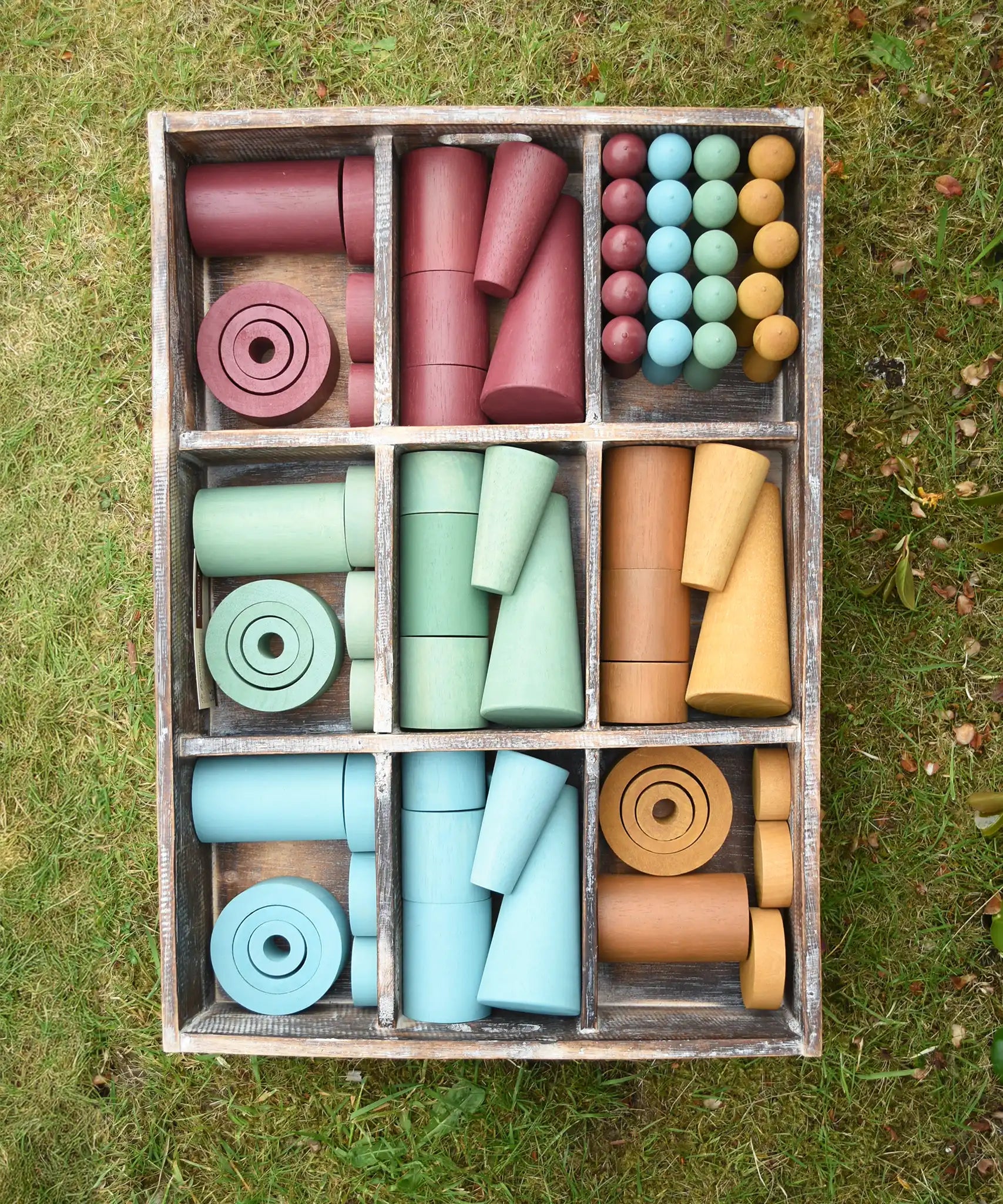 Papoose Toys wooden earth tinker tray school set placed on grass.