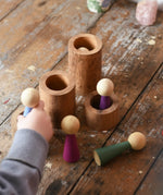 Papoose Toys wooden stacking tubes placed on a wooden surface with Goathe rainbow people placed on and inside the tubes.