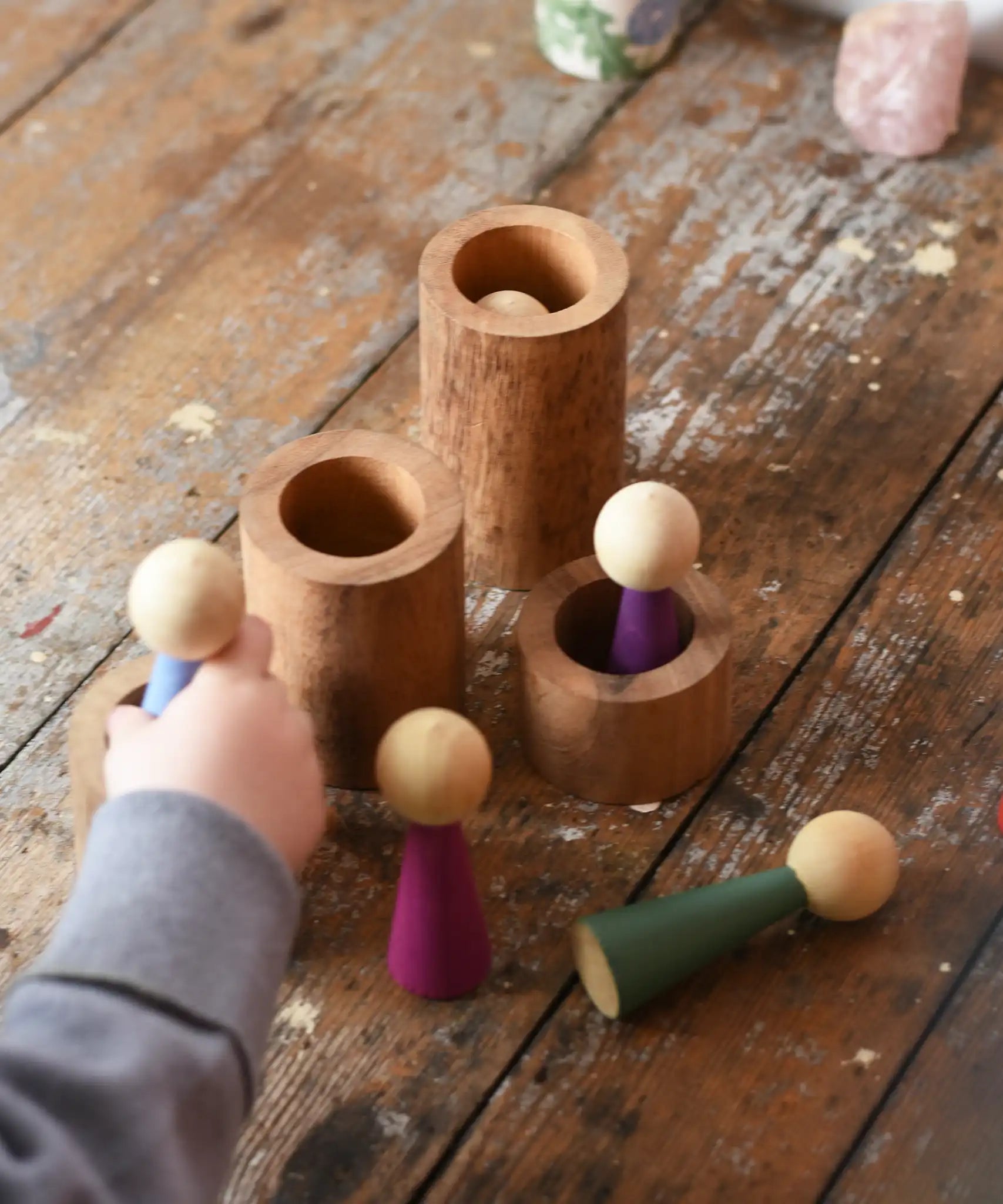 Papoose Toys wooden stacking tubes placed on a wooden surface with Goathe rainbow people placed on and inside the tubes.