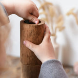 Child playing with Papoose Toys wooden stacking tubes placing something inside one tube.