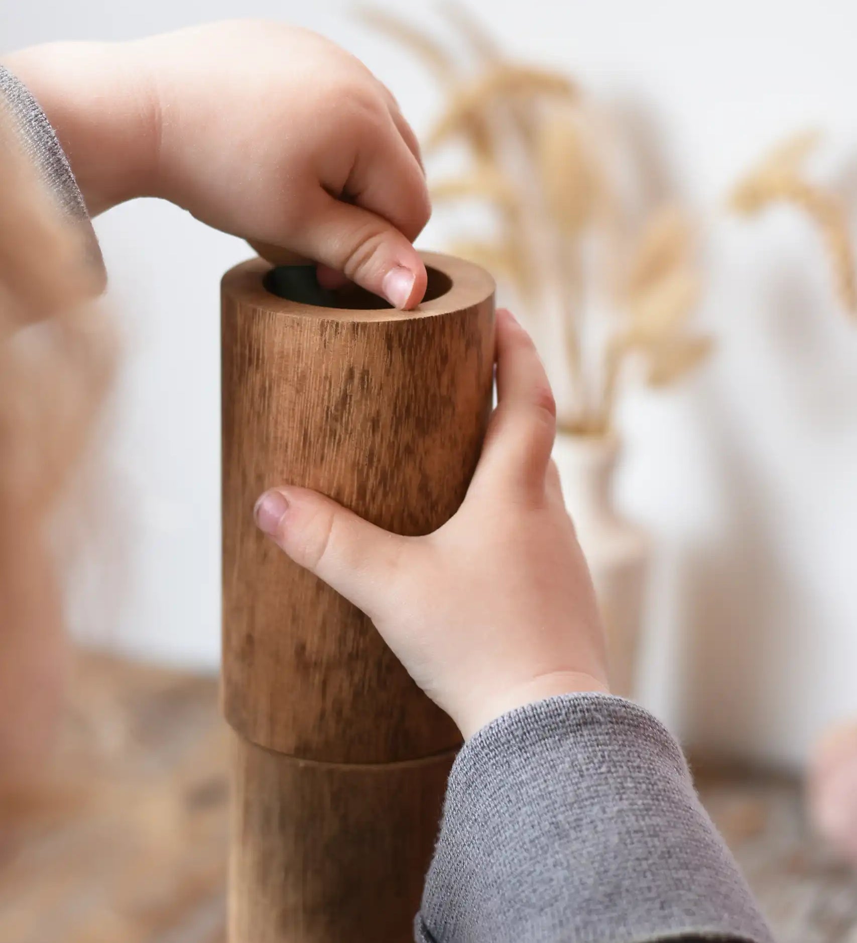 Child playing with Papoose Toys wooden stacking tubes placing something inside one tube.