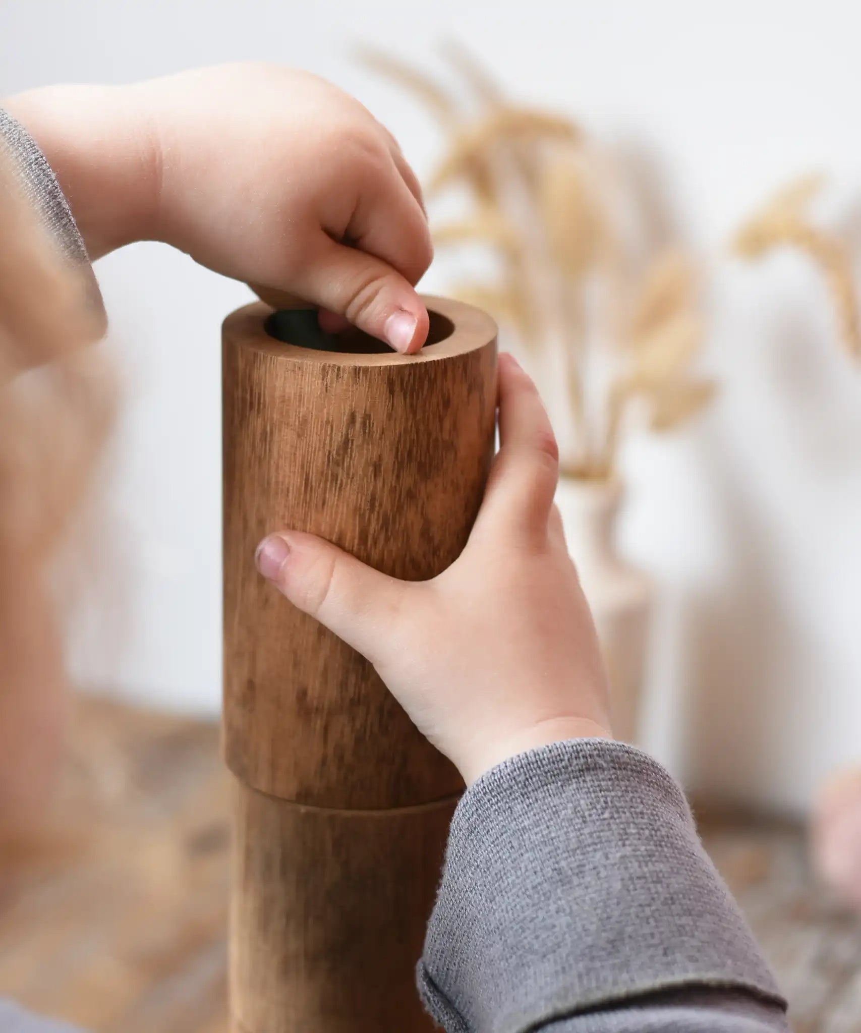Child playing with Papoose Toys wooden stacking tubes placing something inside one tube.